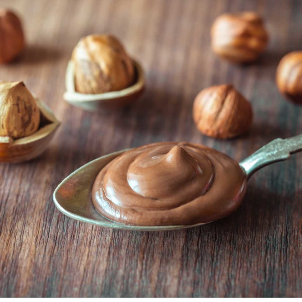 Spoonful of Hazelnut Praliné on a table with hazelnuts in the background